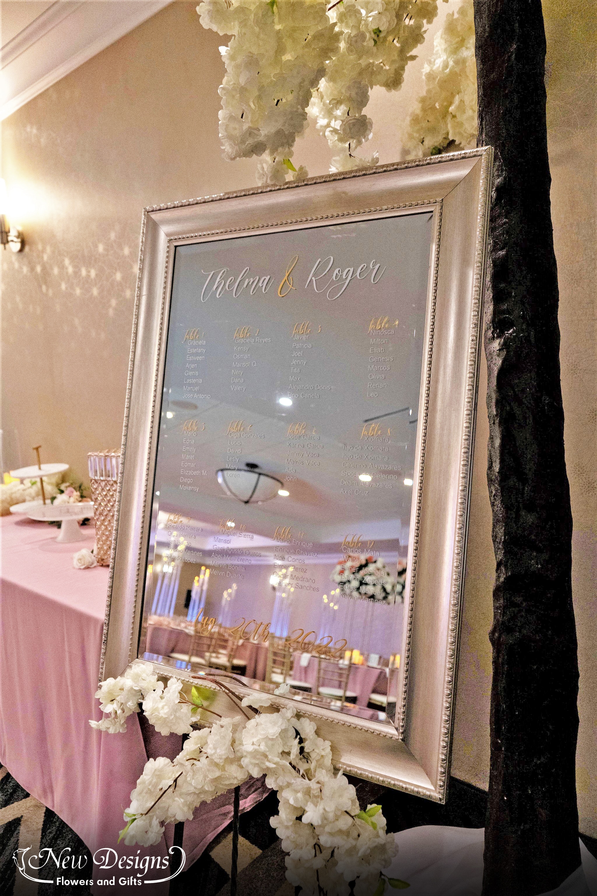 A glass mirror seating chart sits against a white cherry blossom tree installment.